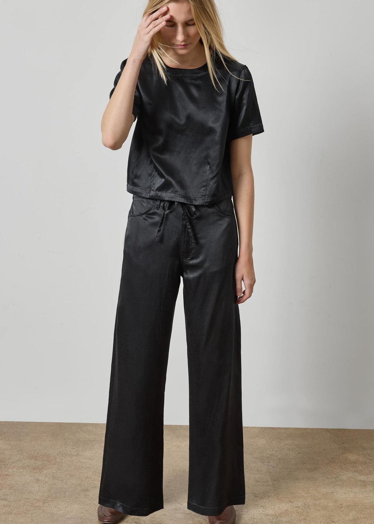 Woman wearing a black satin outfit against a plain background