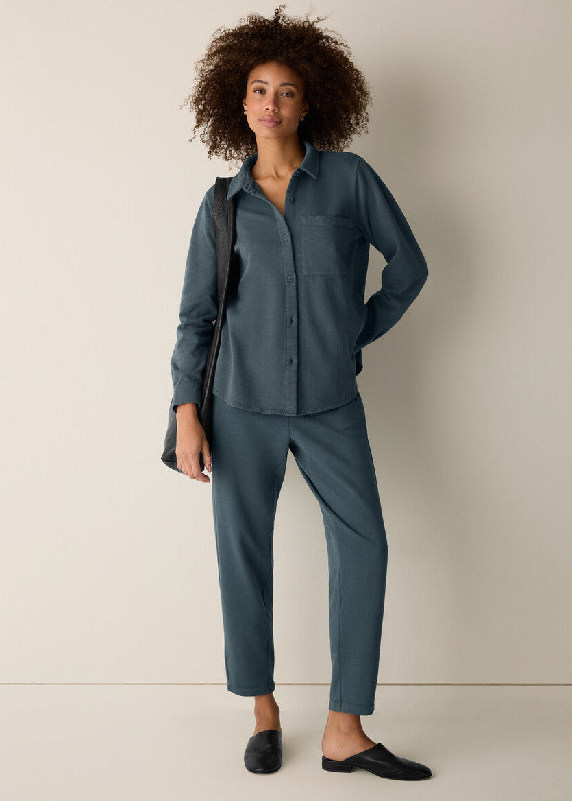 Woman wearing a teal shirt and pants against a beige background