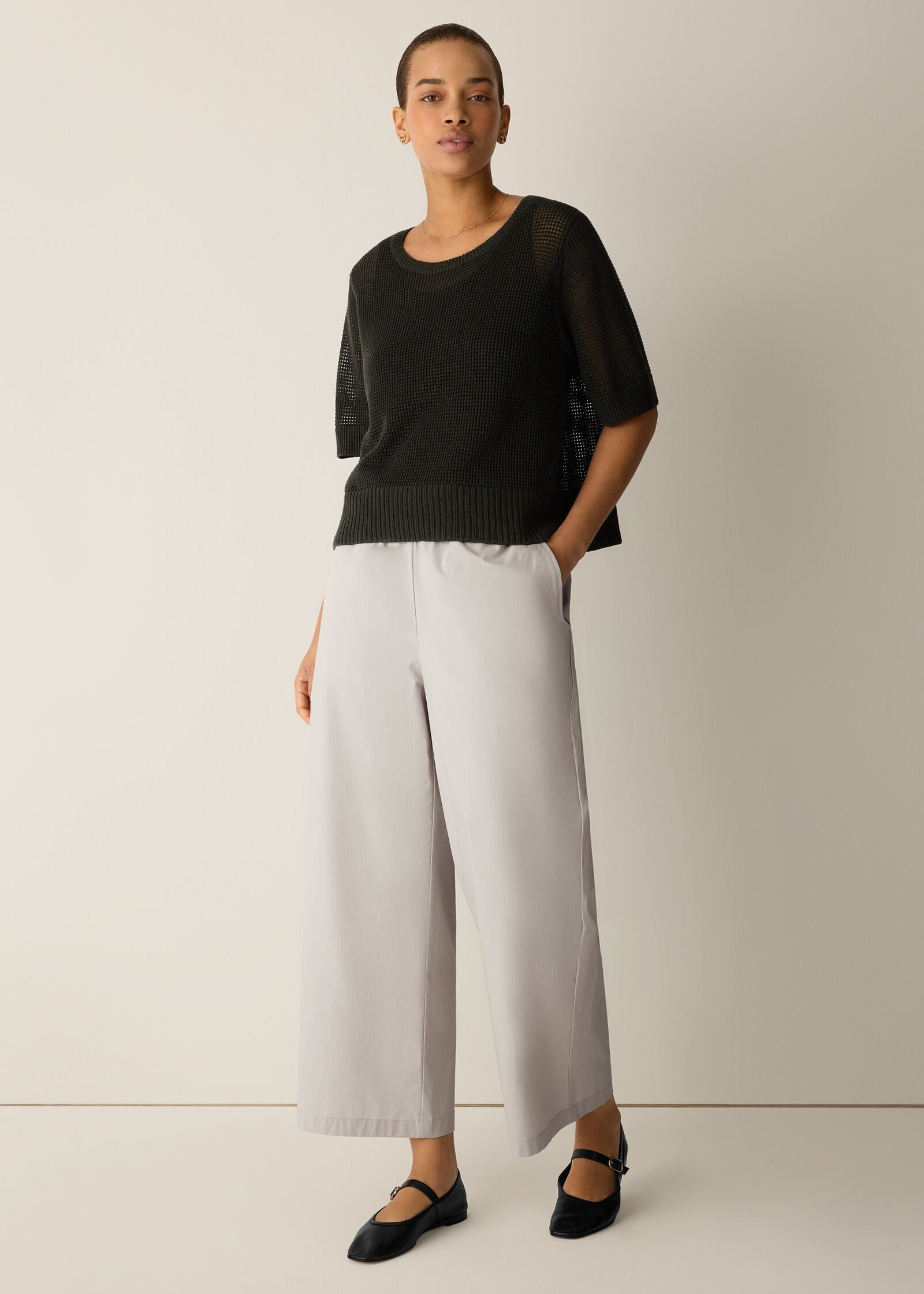 Woman wearing a black top and light gray wide-leg pants on a plain background