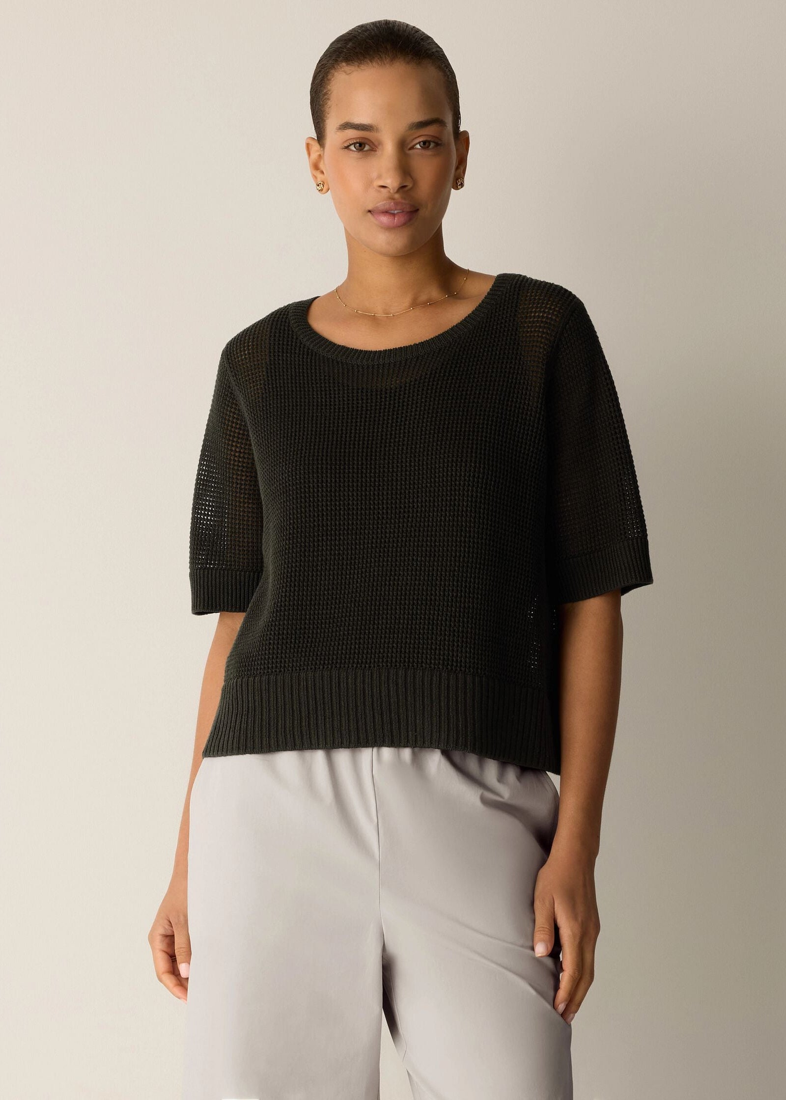 Woman wearing a black sweater and light gray pants against a neutral background
