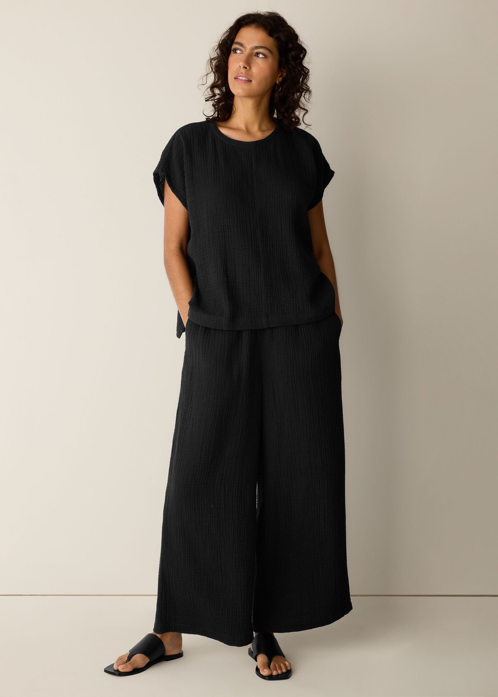 Woman wearing a black outfit with wide-leg pants against a neutral background