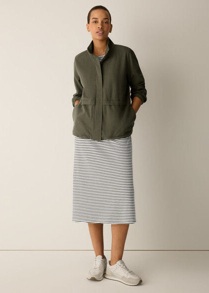 Woman wearing a green jacket and striped skirt against a plain background