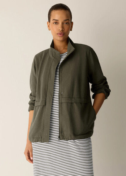 Woman wearing an olive green jacket over a striped dress on a beige background