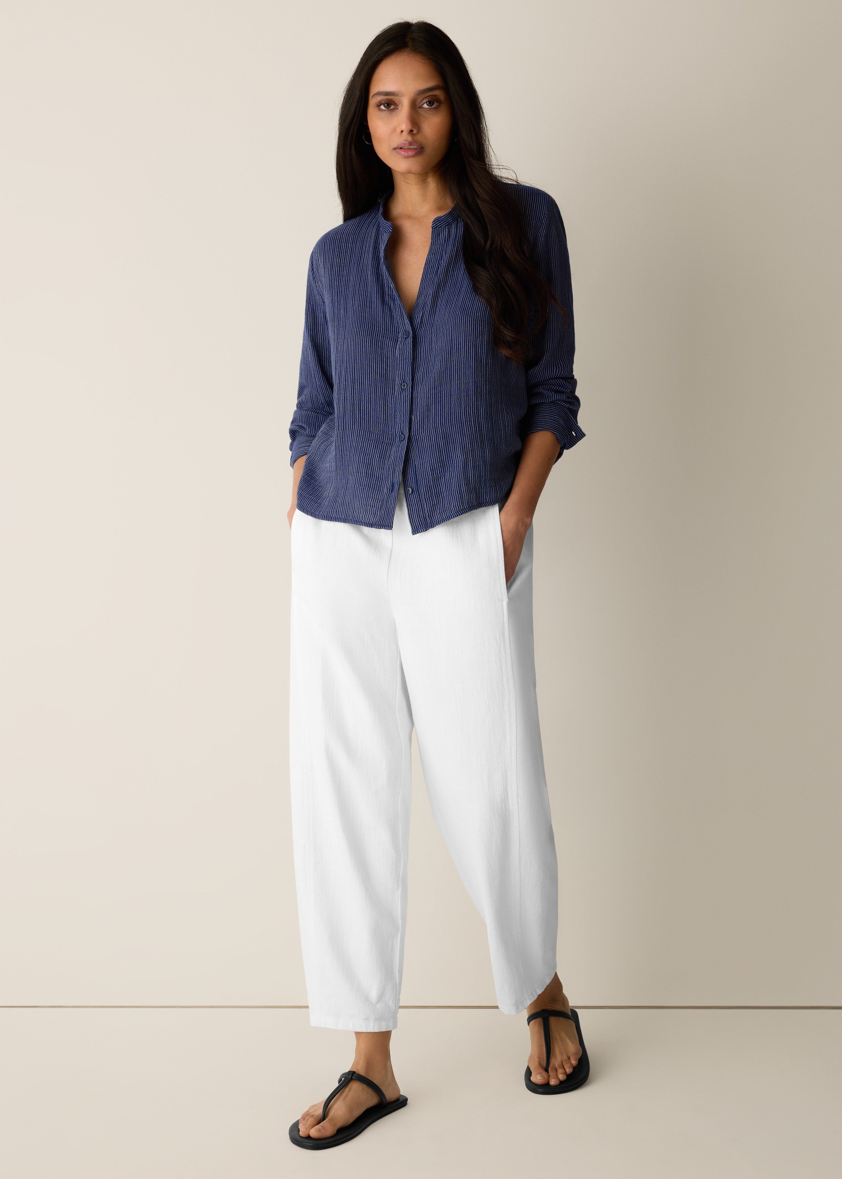 Woman wearing a blue shirt and white pants on a beige background