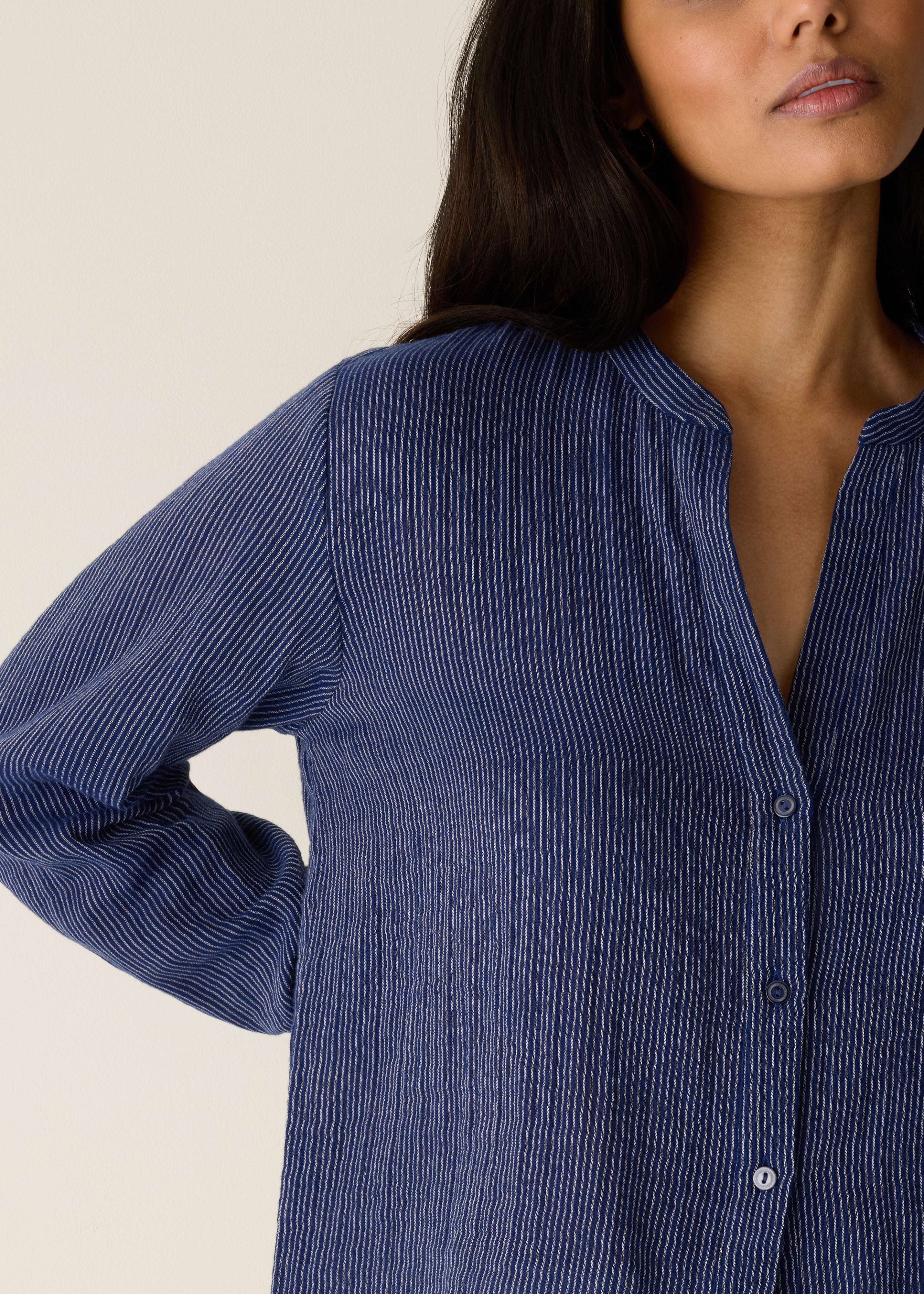Woman wearing a blue striped shirt against a beige background