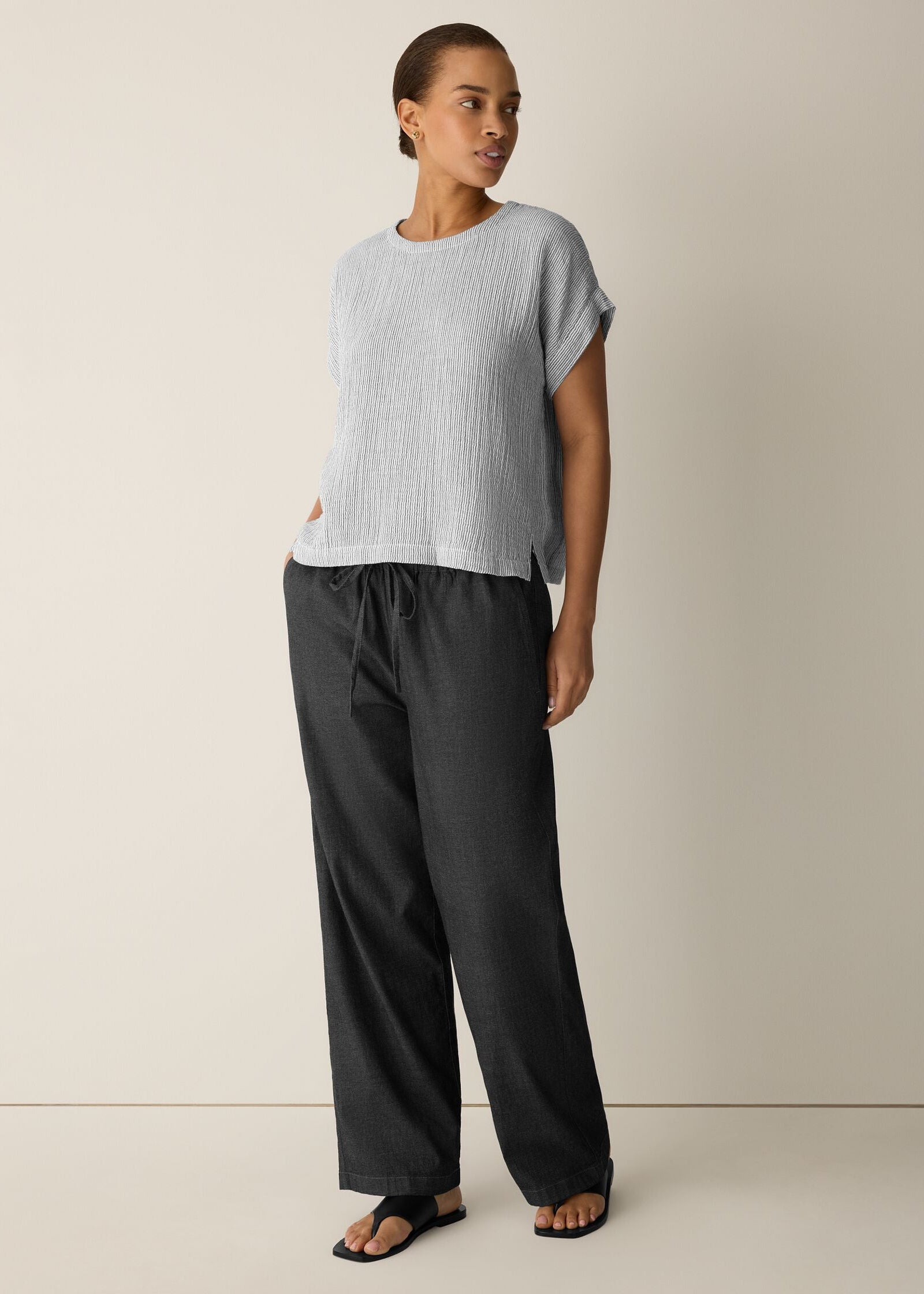 Woman wearing a light gray top and dark gray pants on a beige background