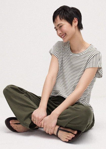 Person wearing a striped shirt and green pants sitting on a white background
