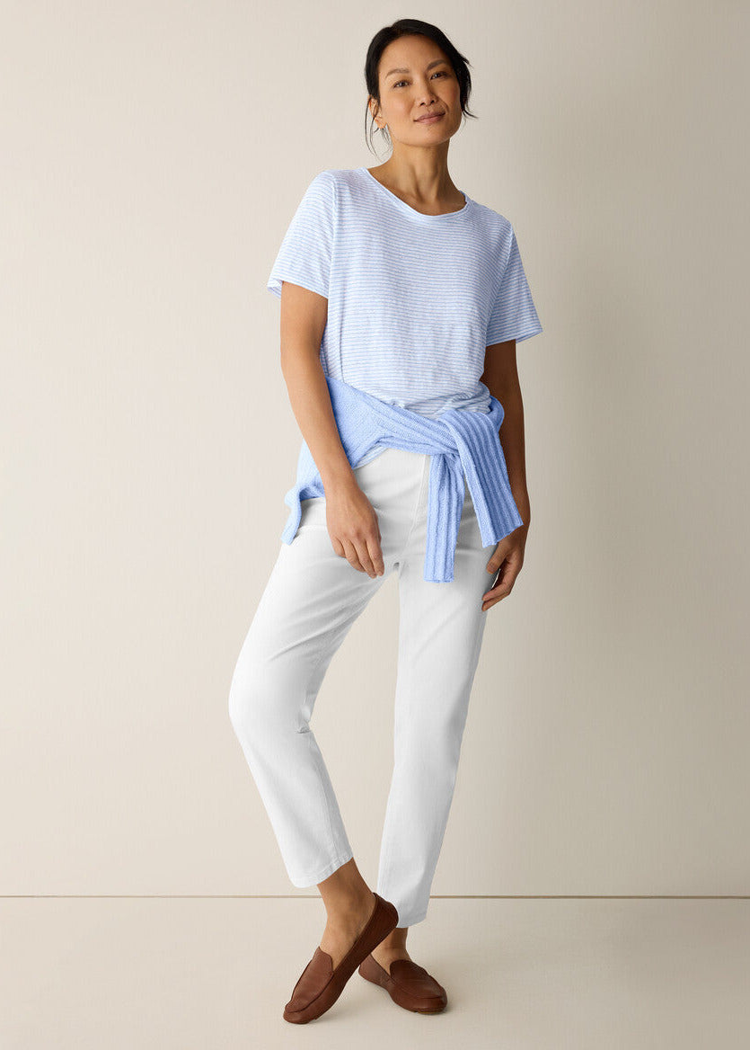 Woman wearing a light blue top and white pants against a beige background