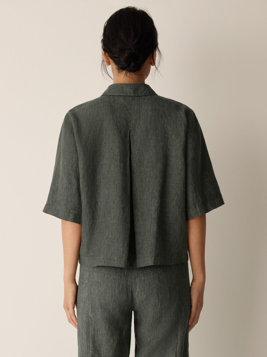 Person wearing a dark green short-sleeve jacket and pants on a beige background
