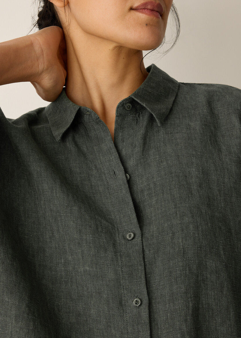 Close-up of a person wearing a dark gray button-up shirt against a neutral background
