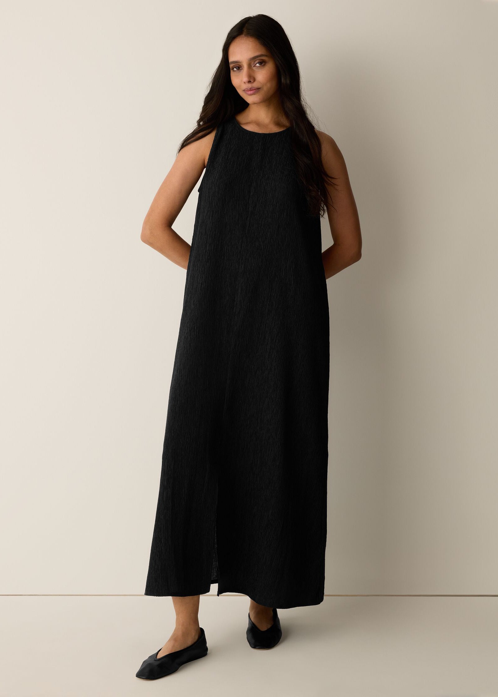Woman wearing a black sleeveless dress against a plain background