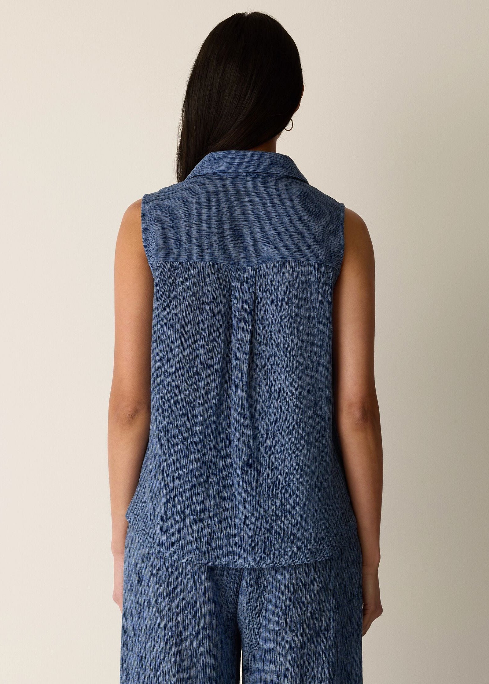 Woman wearing a blue sleeveless top and pants against a beige background