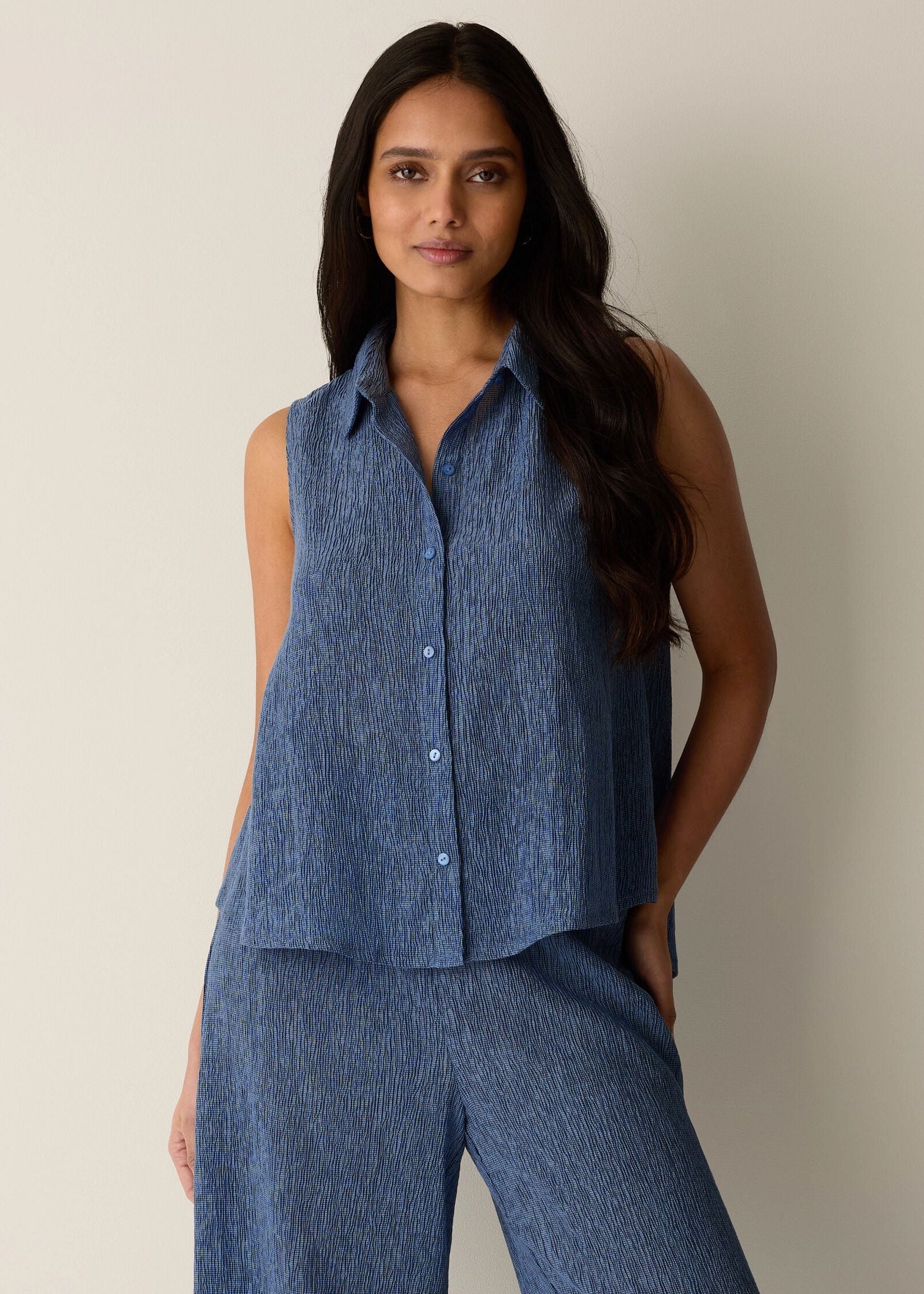 Woman wearing a blue sleeveless top and pants against a neutral background