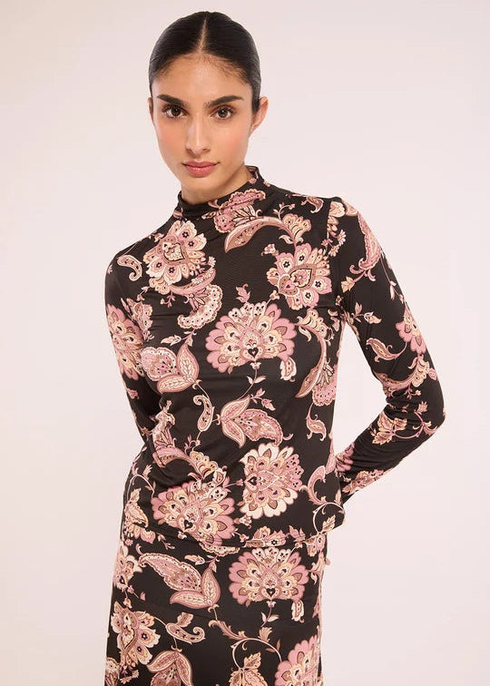A woman modeling a long-sleeve mock-neck dress with a black base and a pink paisley floral pattern, set against a plain light background.