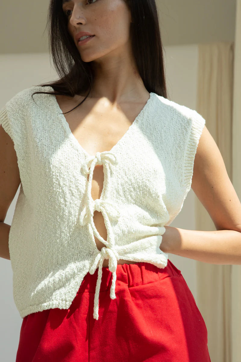 Woman wearing a white sleeveless top with lace-up front and red pants.