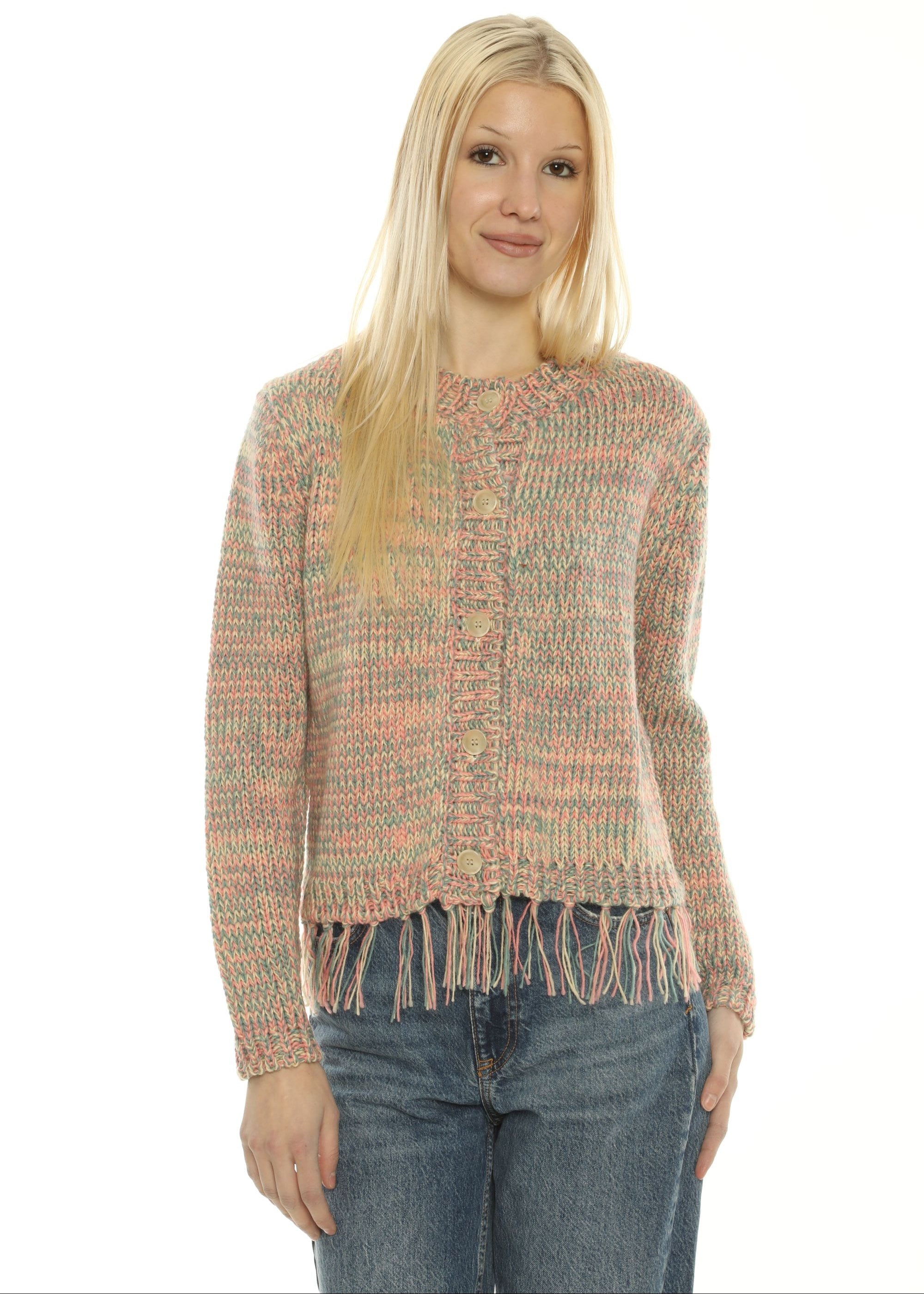 A woman wearing a textured, multicolor knit sweater with fringe trim and blue jeans, photographed against a plain white background.