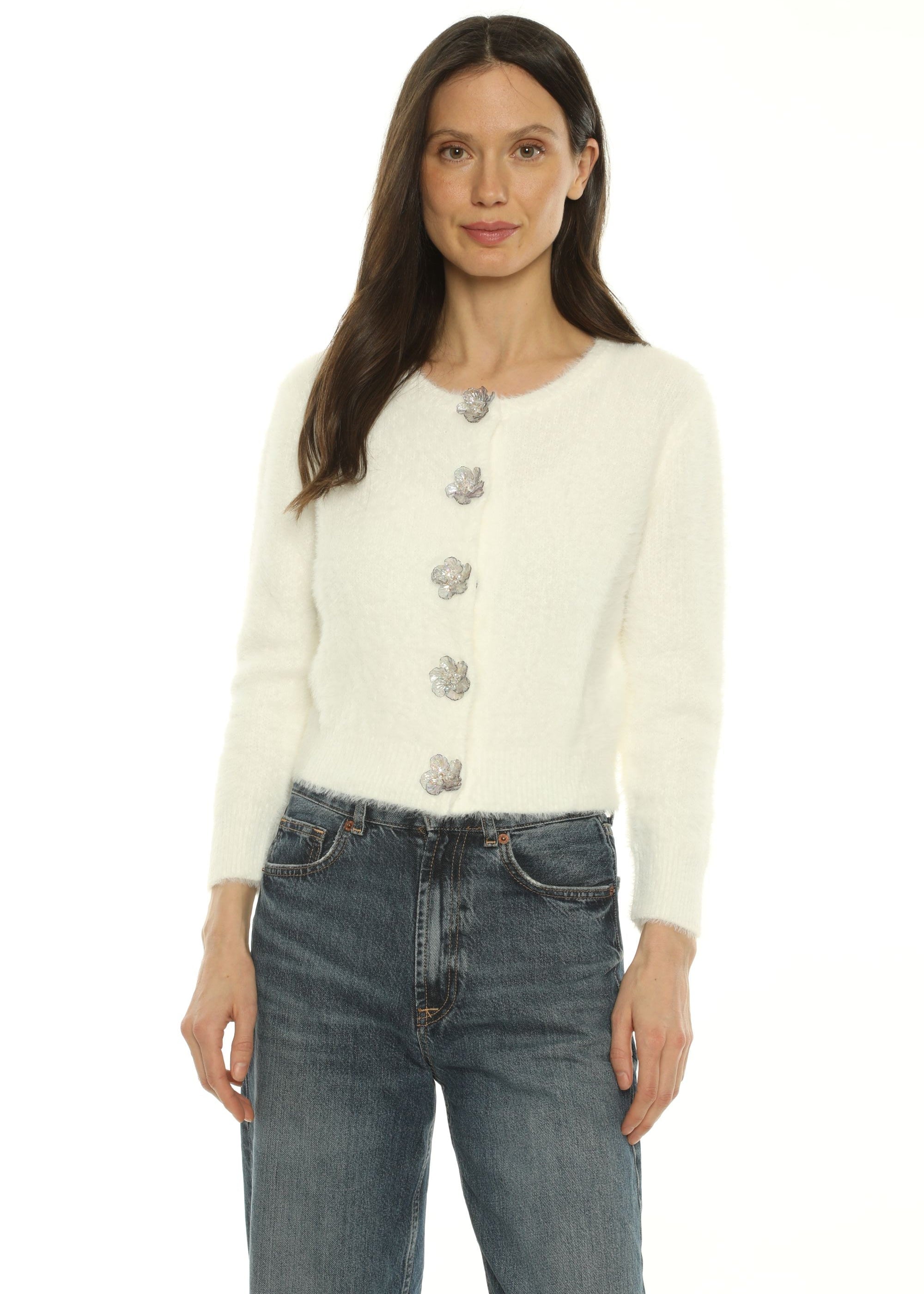A woman wearing a cream-colored knit cardigan with silver floral buttons and blue jeans, shown from a side profile against a plain white background.