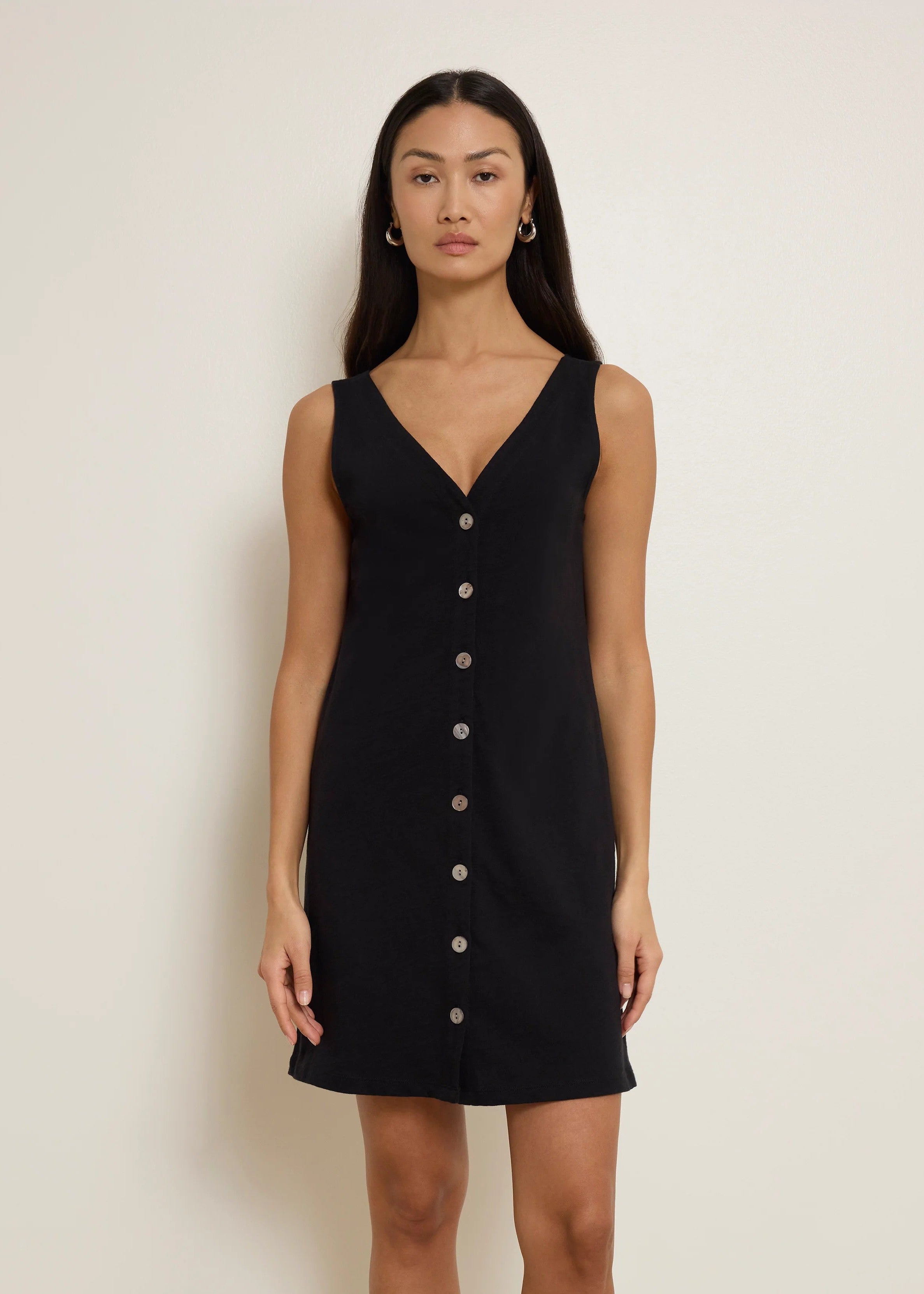 Woman wearing a black sleeveless dress with buttons on a plain background