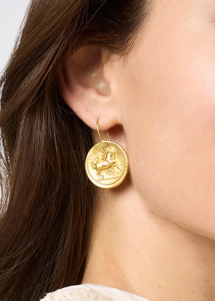 Close-up of a woman wearing a gold earring with a zodiac symbol on a plain background