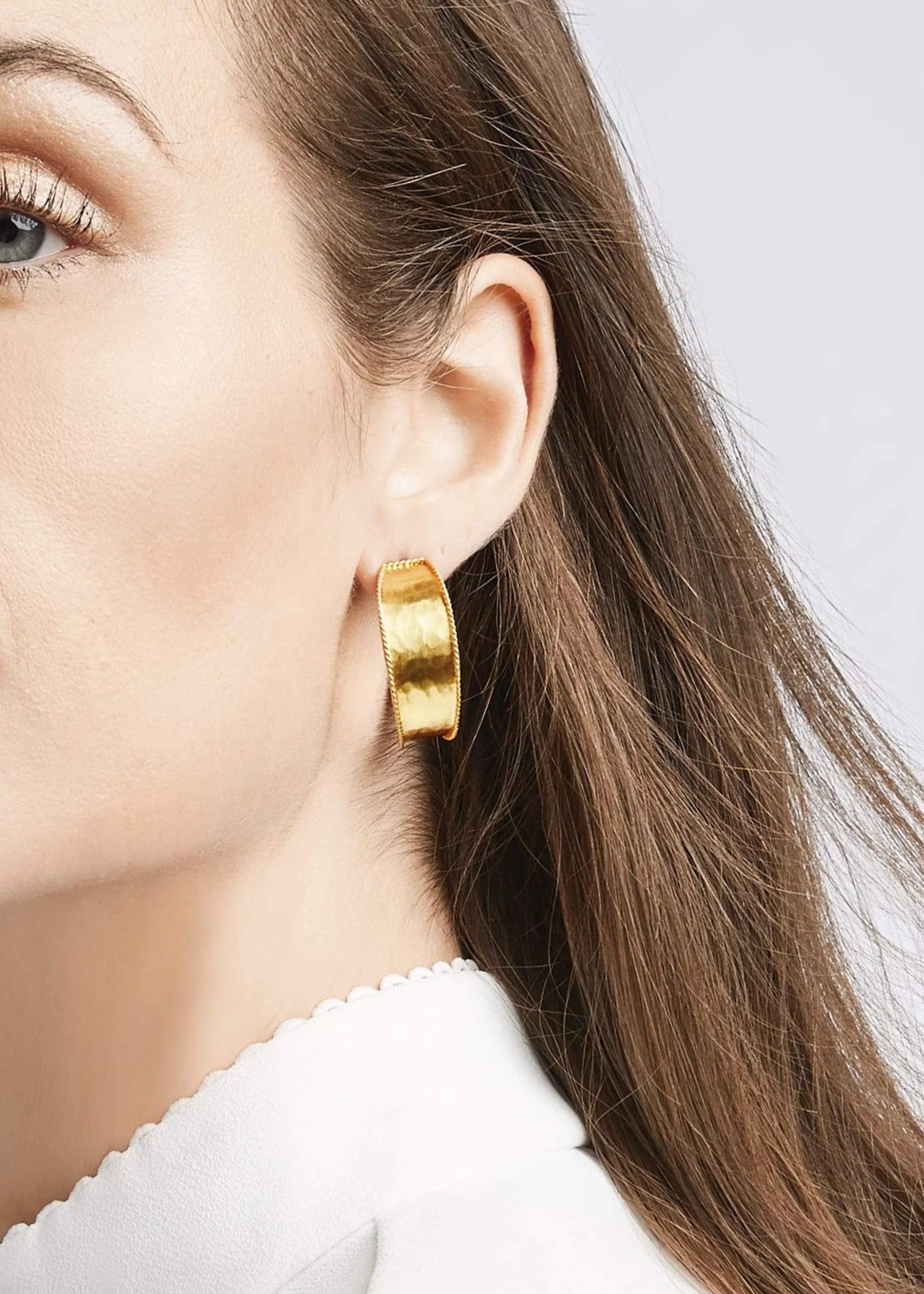 Close-up of a woman wearing gold hoop earrings with a plain background