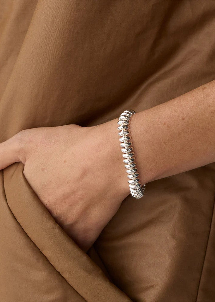 Silver bracelet on a wrist with a brown fabric background
