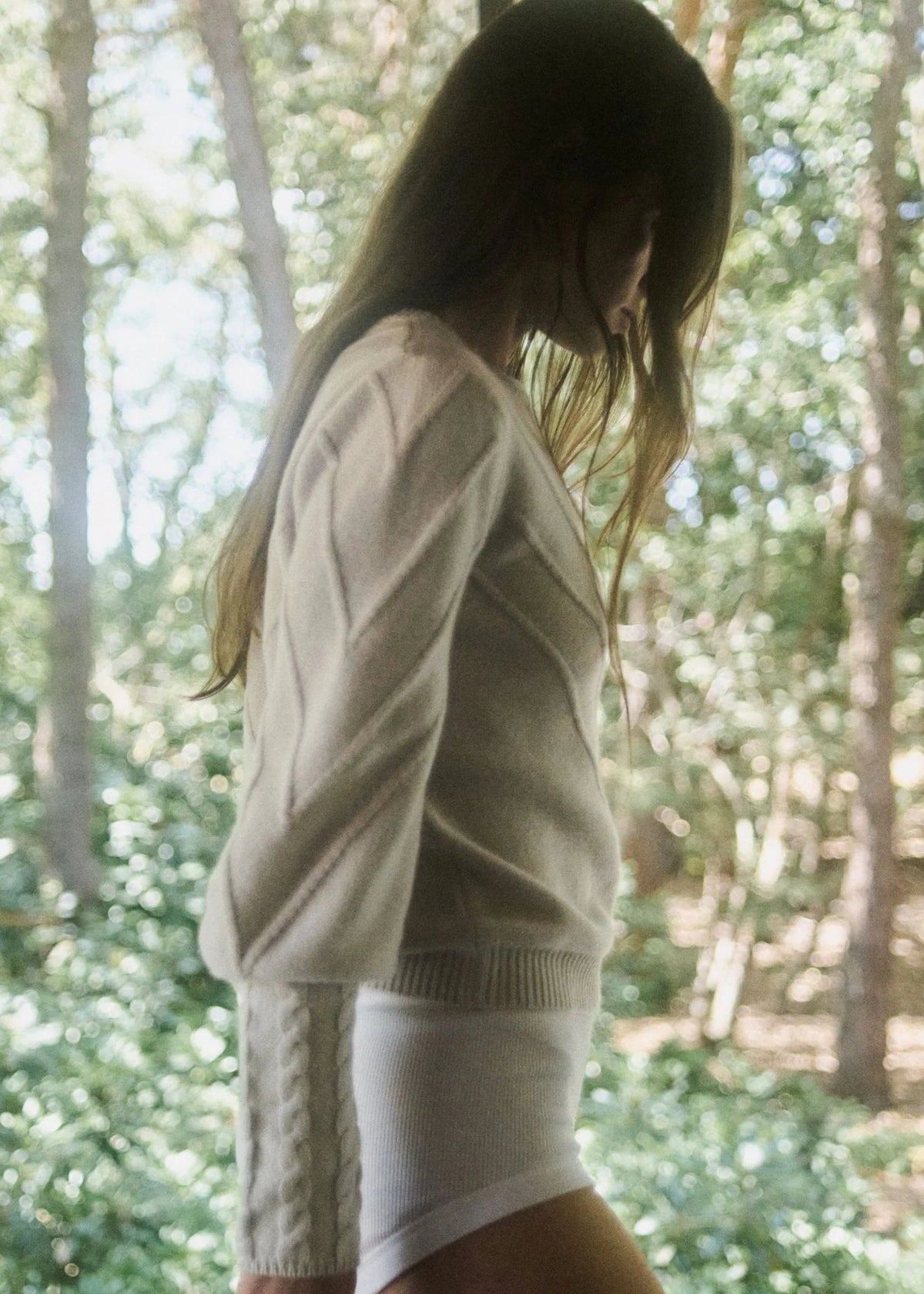 Woman wearing a beige cable knit sweater in a forest setting