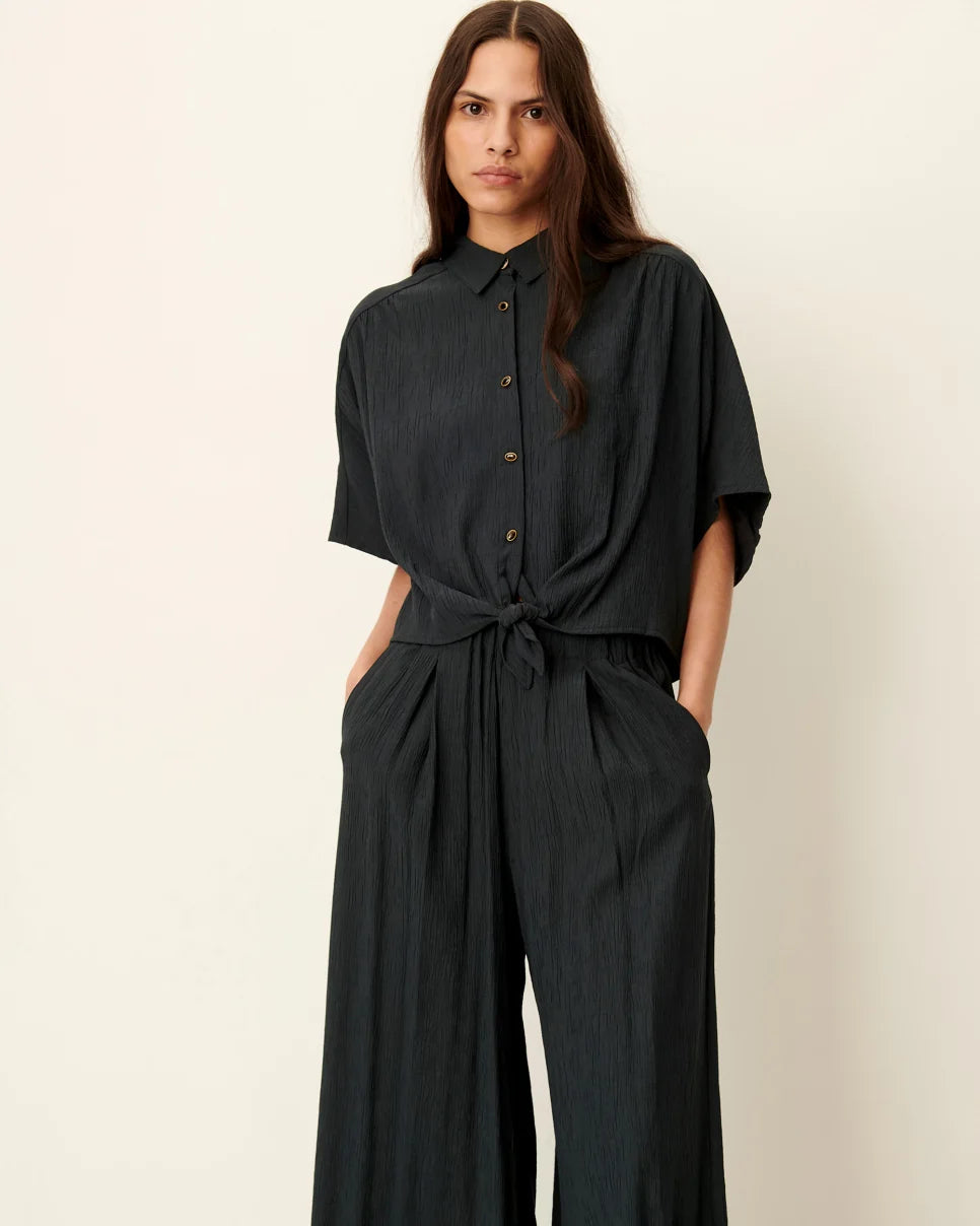 Woman wearing a black jumpsuit against a beige background