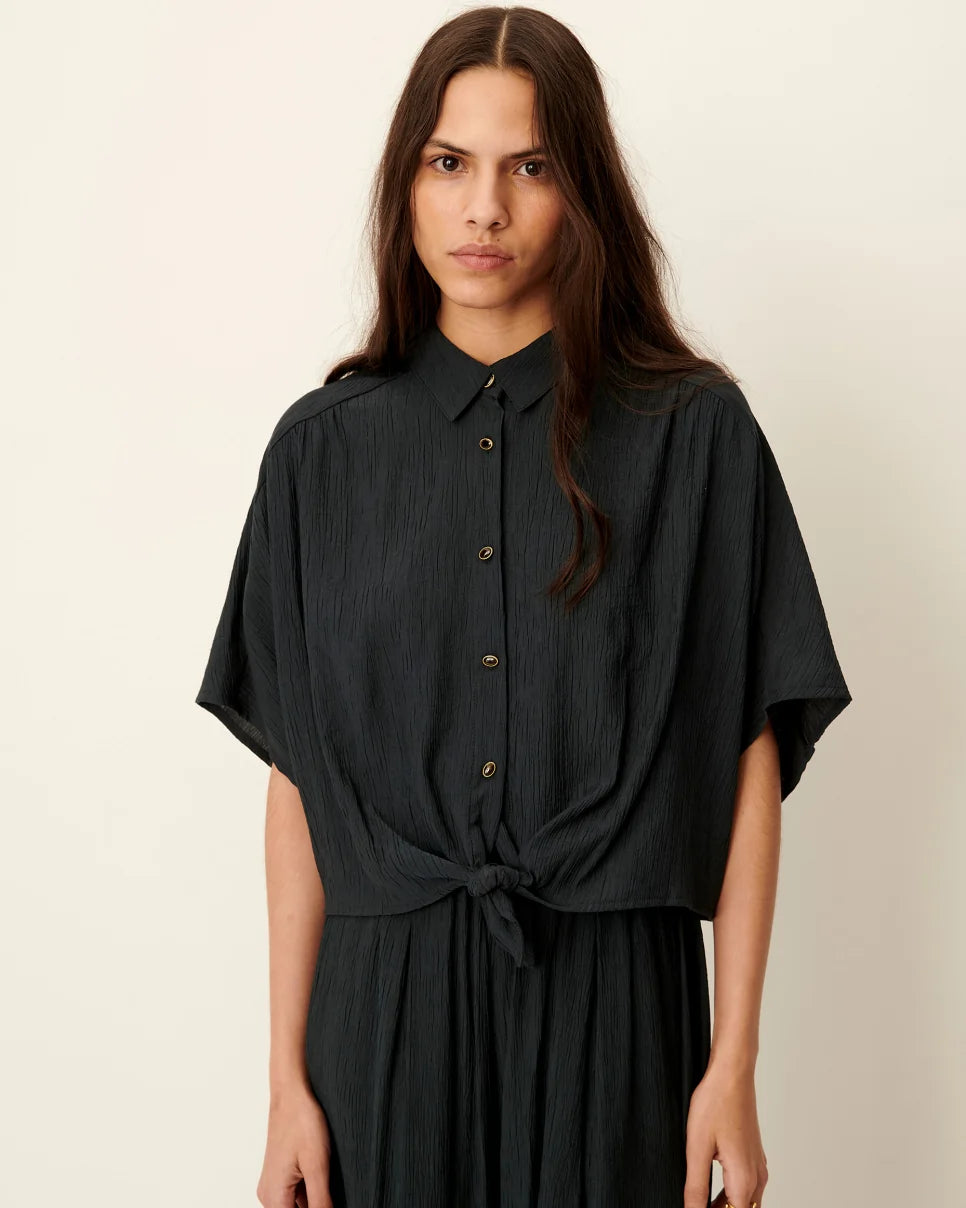 Woman wearing a black dress with short sleeves against a beige background