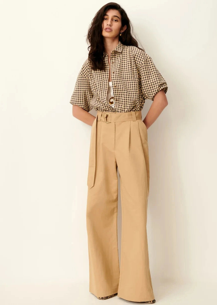 Woman wearing a checkered blouse and beige wide-leg pants on a white background