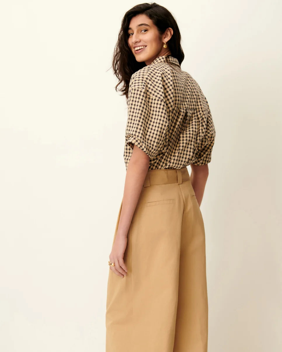Woman wearing a checkered blouse and beige pants on a plain background