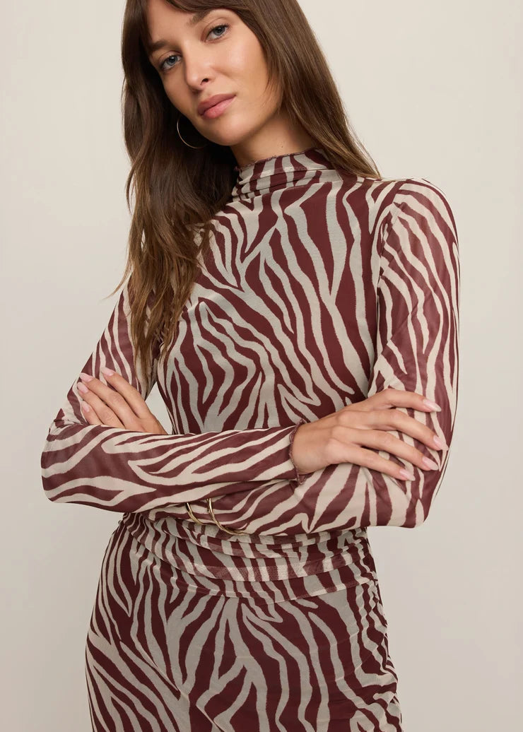 A woman wearing a long-sleeve mock-neck dress with a brown and beige zebra print, posed against a neutral light beige background.