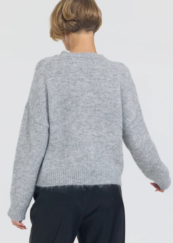 Person wearing a gray sweater and dark pants on a white background