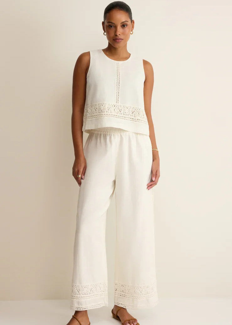 Woman wearing a white sleeveless top and wide-leg pants against a beige background