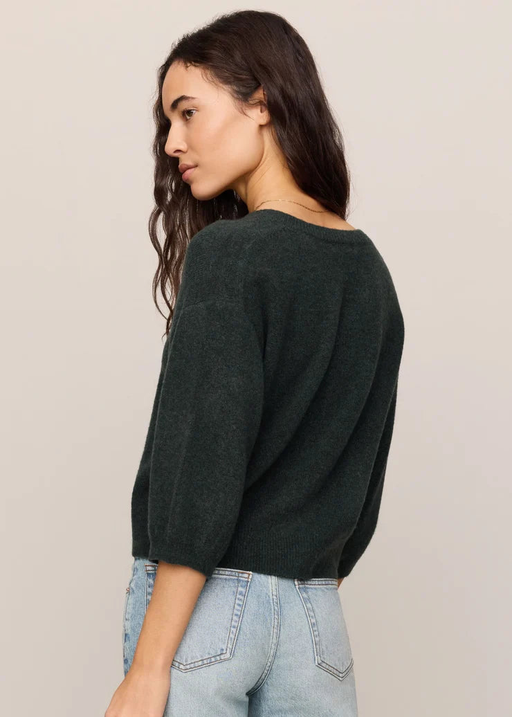 Woman wearing a dark green sweater and light blue jeans against a plain background