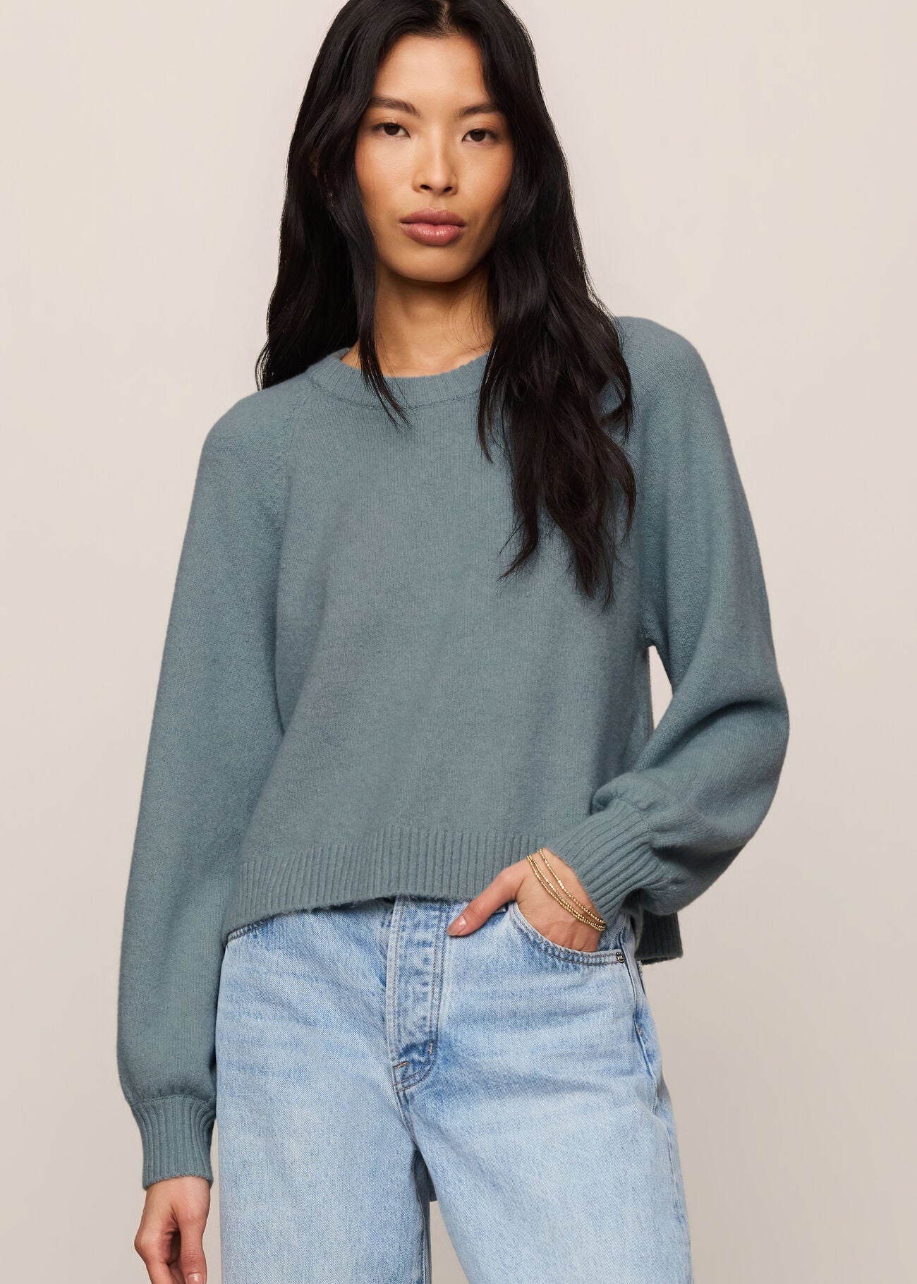 Woman wearing a teal sweater and light blue jeans against a beige background