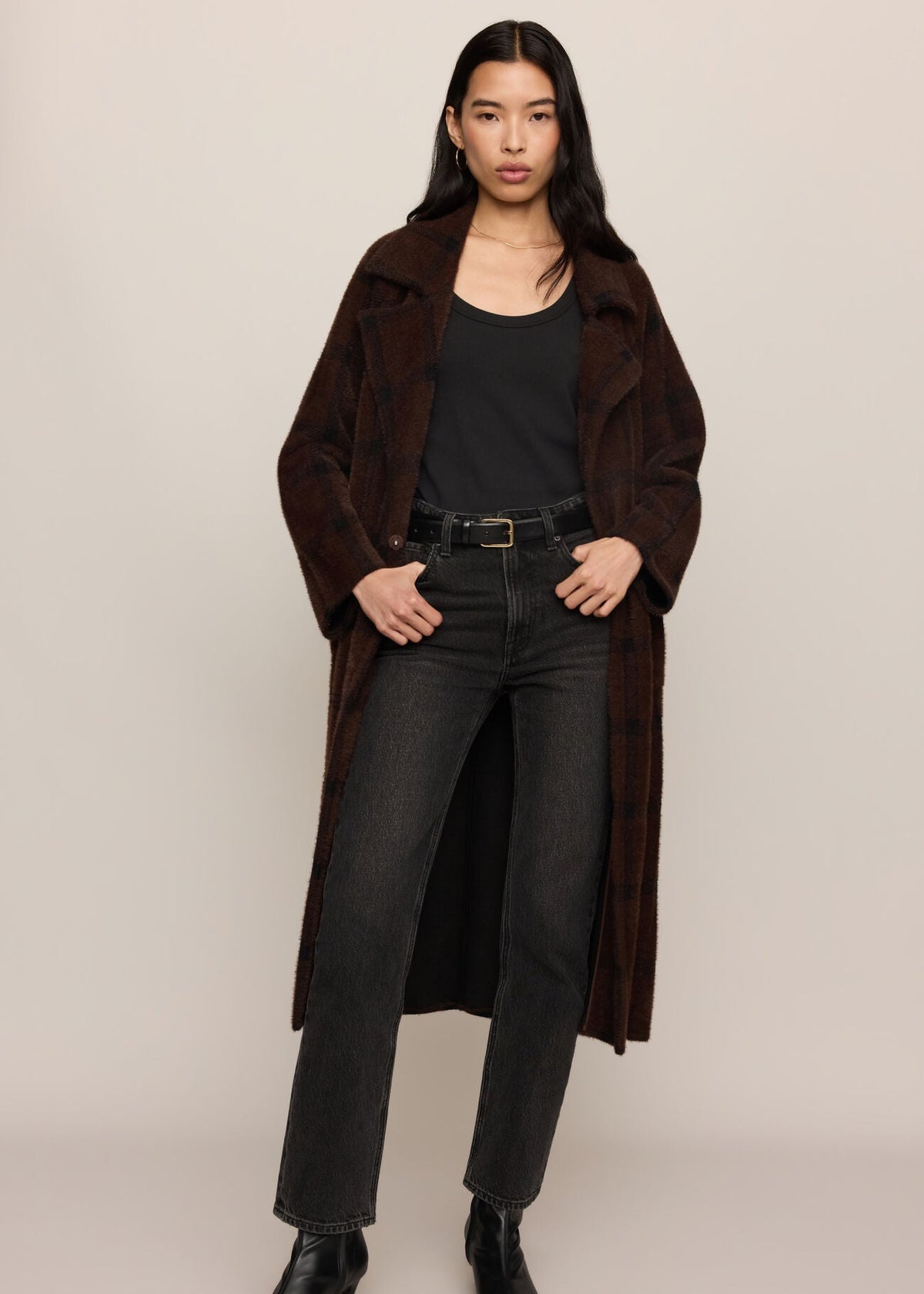 Woman wearing a brown coat, black top, and jeans on a beige background