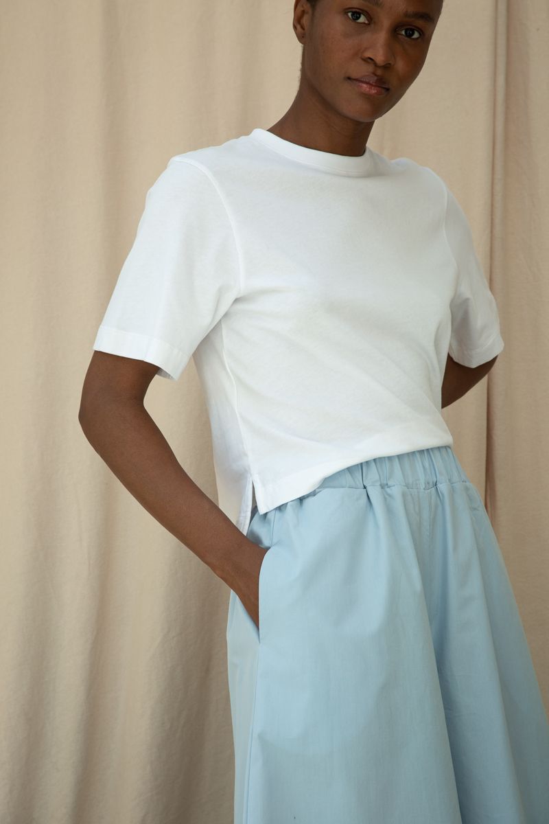 Person wearing a white top and light blue pants against a beige background