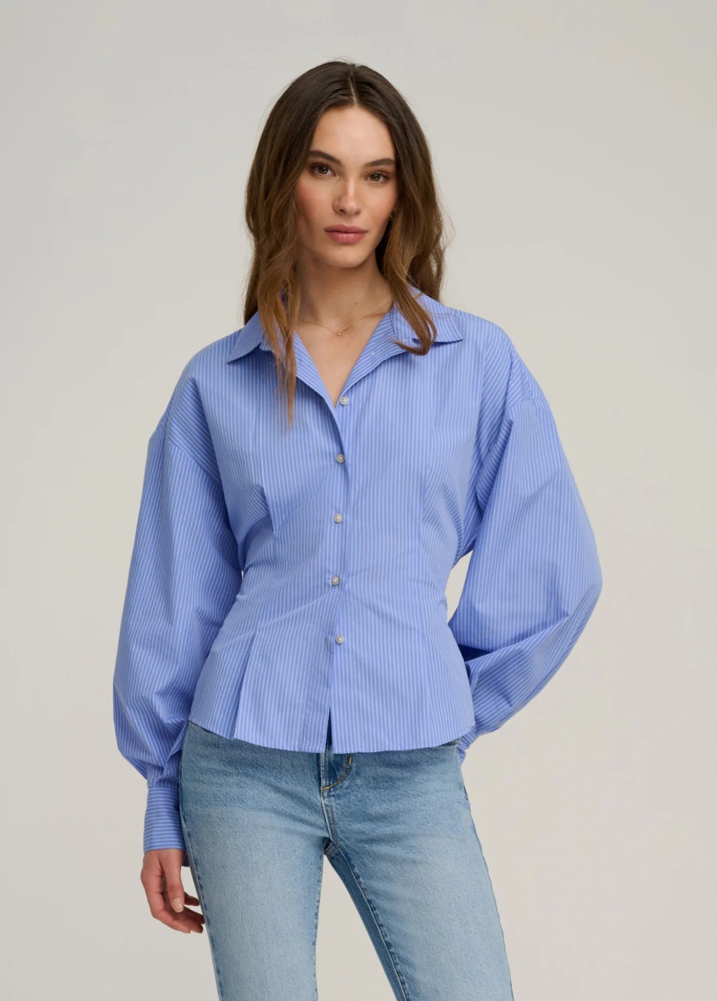 Woman wearing a blue striped shirt and jeans against a plain background