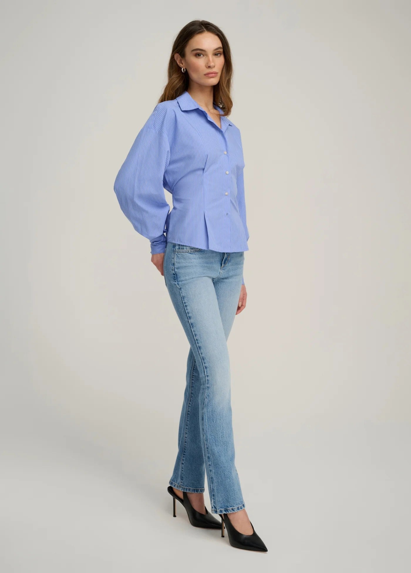 Woman wearing a light blue blouse and jeans on a plain background