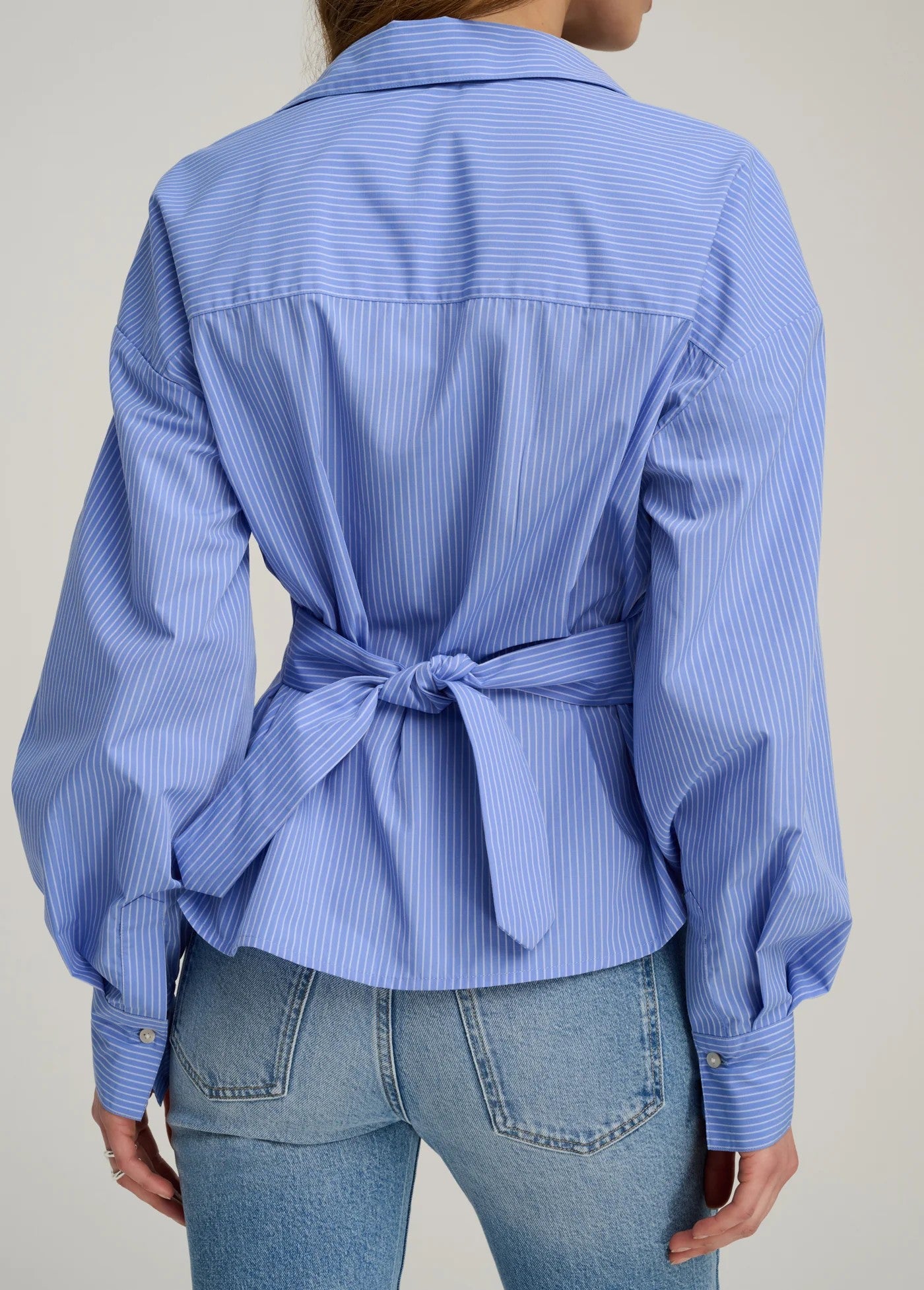 Blue striped shirt tied at the waist with light blue jeans on a neutral background