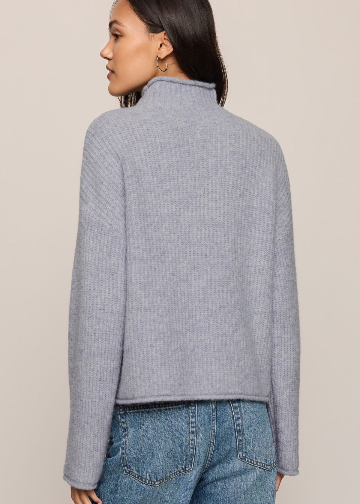 Woman wearing a gray textured sweater and blue jeans on a beige background