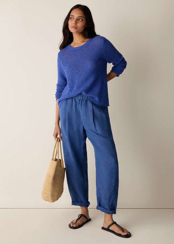 Woman wearing a blue outfit holding a beige bag against a neutral background
