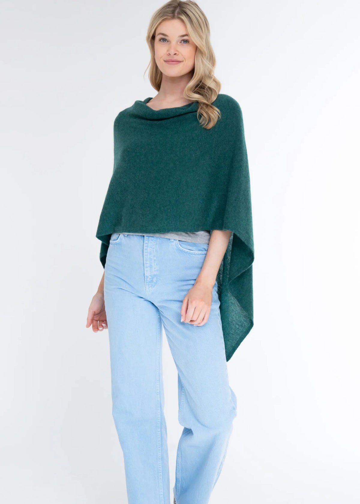 Woman wearing a green poncho and light blue jeans on a white background