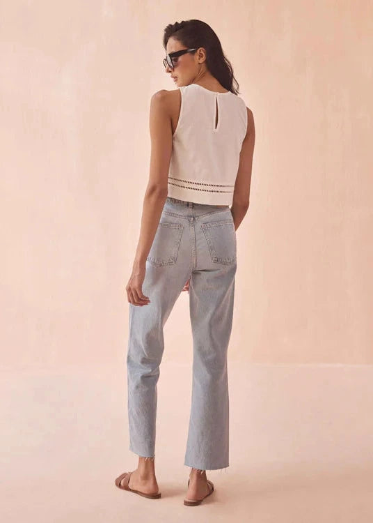 Woman wearing a sleeveless top and light blue pants on a beige background