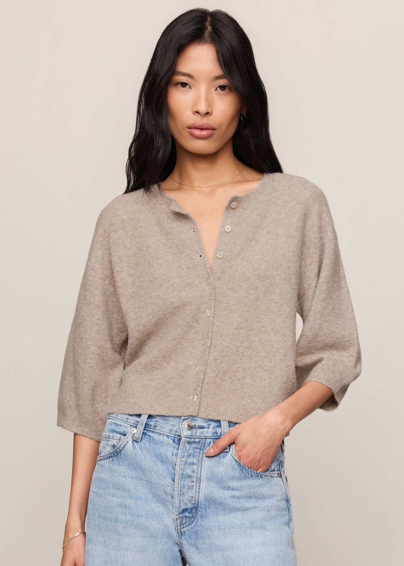 Woman wearing a beige cardigan and light blue jeans against a plain background