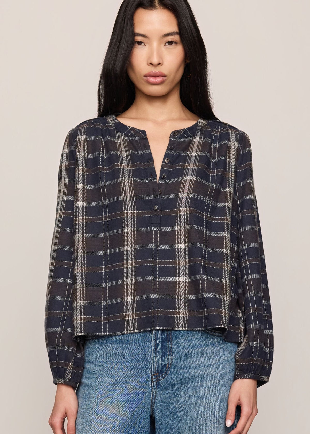 Woman wearing a plaid shirt and jeans against a plain background