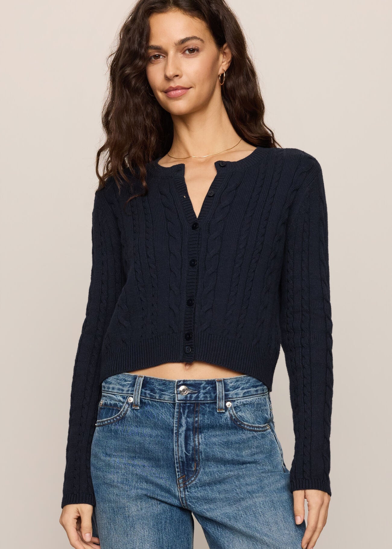 Woman wearing a navy blue cardigan and blue jeans on a beige background