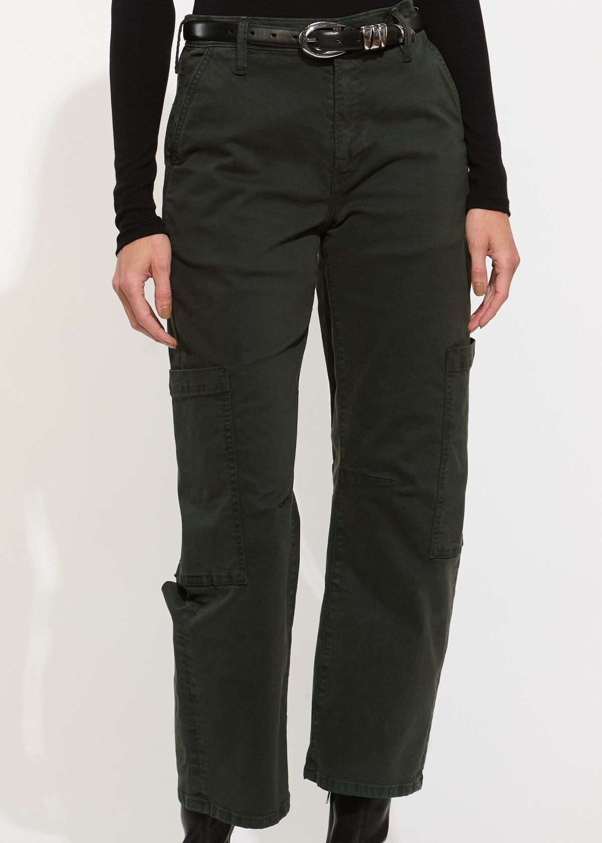 A model wearing dark olive green cargo pants with a black belt, paired with a black long-sleeve top and black ankle boots, shown from the waist down against a white studio background.