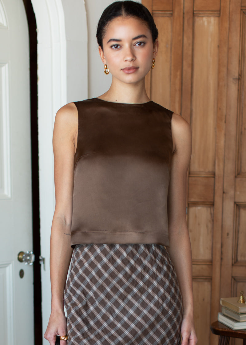 Woman wearing a brown top and plaid skirt standing indoors.