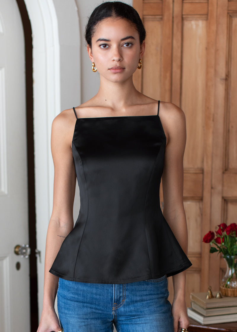 Woman wearing a black peplum top and blue jeans indoors.